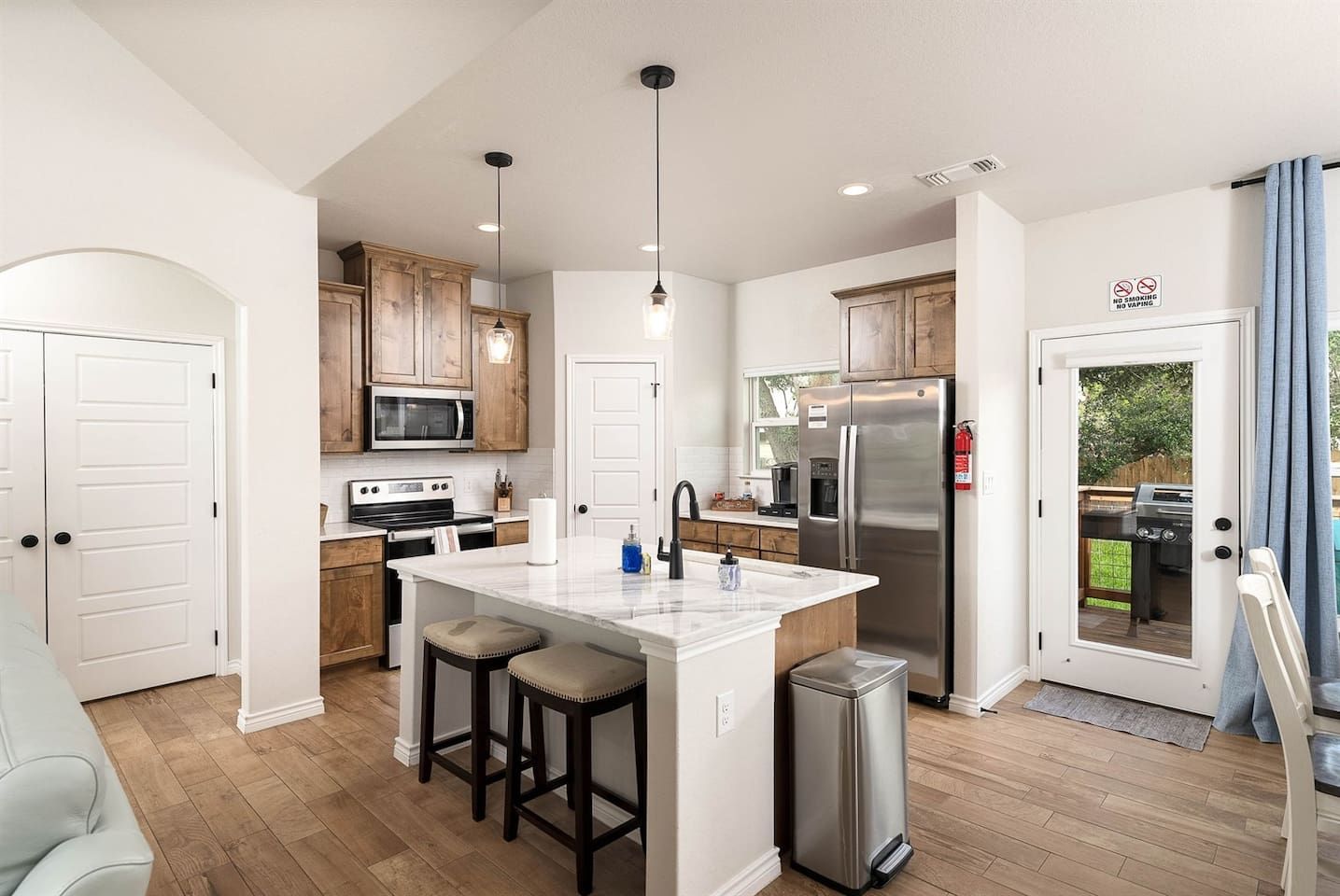 A modern kitchen with wooden cabinets, stainless steel appliances, and a central island with stools.