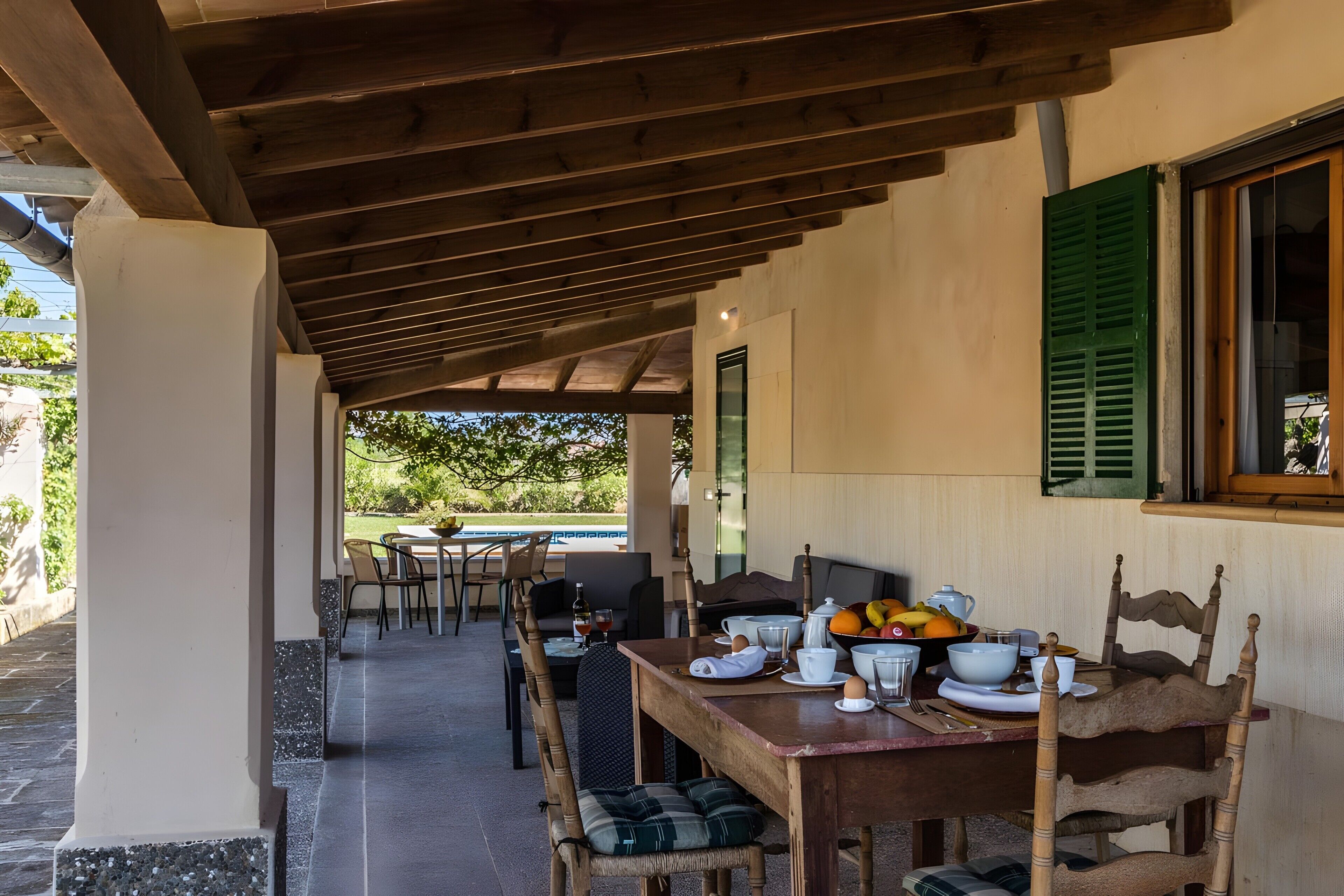 An outdoor dining area with a covered patio, tables, chairs, and a view of a pool.