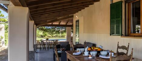 An outdoor dining area with a covered patio, tables, chairs, and a view of a pool.