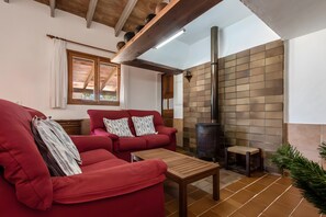 A cozy living room with a red sofa, a small wooden table, and a wood-burning stove. - Holiday Home "Catalina Petit" with Mountain View, Pool, Garden, Terrace & Wi-Fi (Pollença)