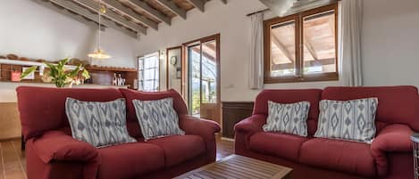 A living room with two red sofas, a wooden coffee table, and a kitchen area with a hanging light fixture.