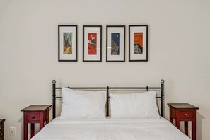 Ein Bett mit weißen Leinentüchern, einem schwarzen Metall-Kopfstück und zwei Nachttischen mit Schubladen.