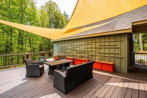Eine Terrasse mit Gartenmöbeln, einem gelben Sonnensegel und einer grünen Wand mit Rasterstruktur.