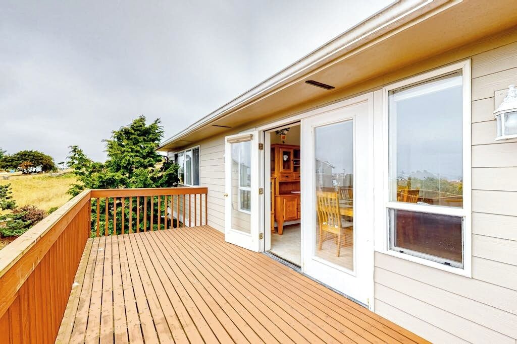 A wooden deck with a glass door leading to a room with a dining table and chairs.