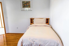 Une chambre à coucher avec un lit en bois, un mur blanc et un tableau accroché au-dessus du lit.