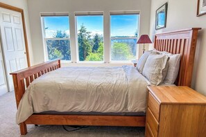 Un dormitorio con cama de madera, una mesita de noche y vistas a árboles a través de amplias ventanas.