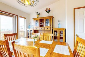 A dining area with a wooden table, chairs, a cabinet with glass doors, and a vase with flowers. - Ocean View Home with Outdoor Living Space, Laundry, and Balcony (Coupeville)