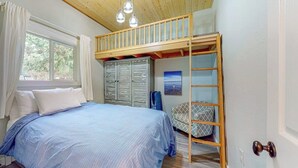Una camera da letto con un letto a castello, un letto con copriletto blu, un armadio e una finestra con tende.