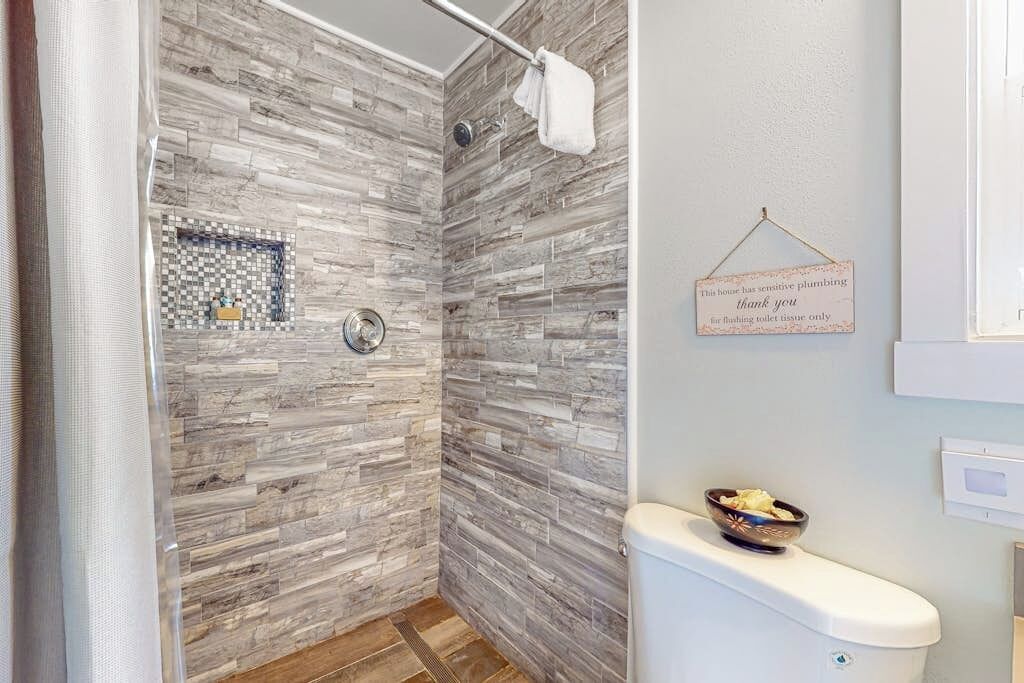 A bathroom with a shower area featuring a mosaic tile wall and a toilet with a bowl of toiletries.