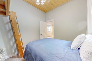 Un dormitorio con una cama, una escalera de madera y una puerta blanca que da a otra habitación.
