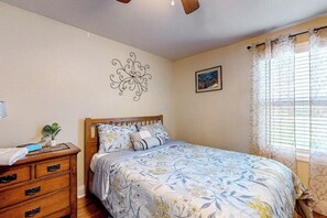 A bedroom with a wooden bed, a nightstand, a wall decoration, and a window with curtains.