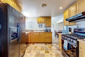 A kitchen with wooden cabinets, a black refrigerator, a stove, and a tiled floor. - Charming Single Level Home with Fireplace, Patio, and Fast WiFi in Oak Harbor (Oak Harbor)