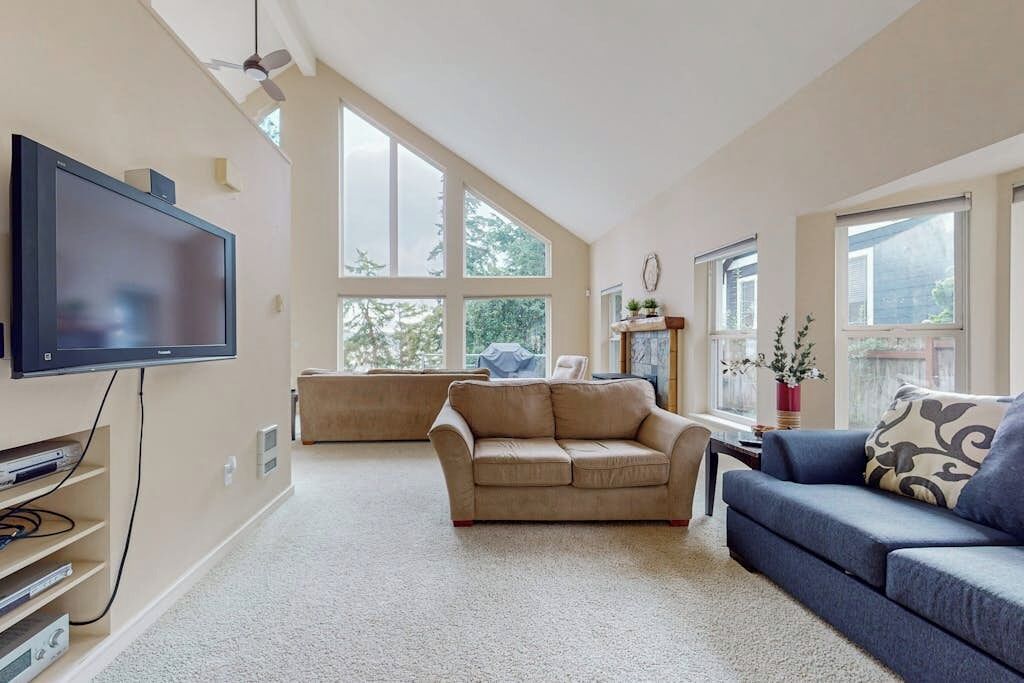 A living room with a flat-screen TV, two sofas, a coffee table, and a large window providing natural light.