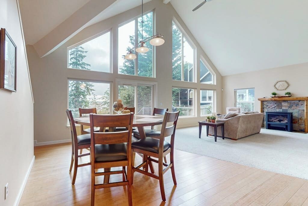 A spacious living room with a high ceiling, large windows, and a fireplace.