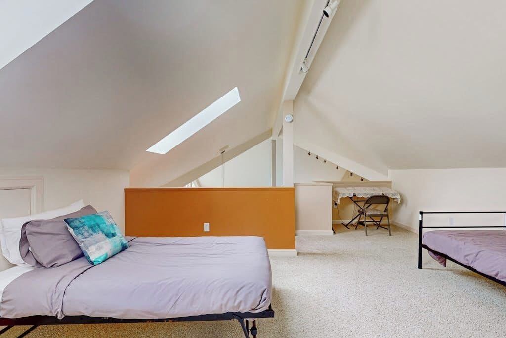 Quarto com teto inclinado, cama, escrivaninha e cadeira.