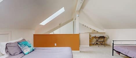 A bedroom with a sloped ceiling, a bed, a desk, and a chair.