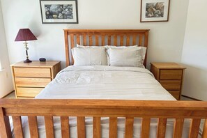 A bed with a wooden headboard, two bedside tables, and a lamp on one of the tables. - Family Friendly Coupeville Holiday Home with Ocean Views Private In Law Suite and Garden Oasis (Coupeville)