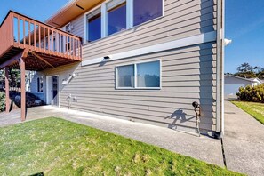 Une maison à deux étages avec une terrasse en bois, une porte d’entrée et une petite fenêtre.