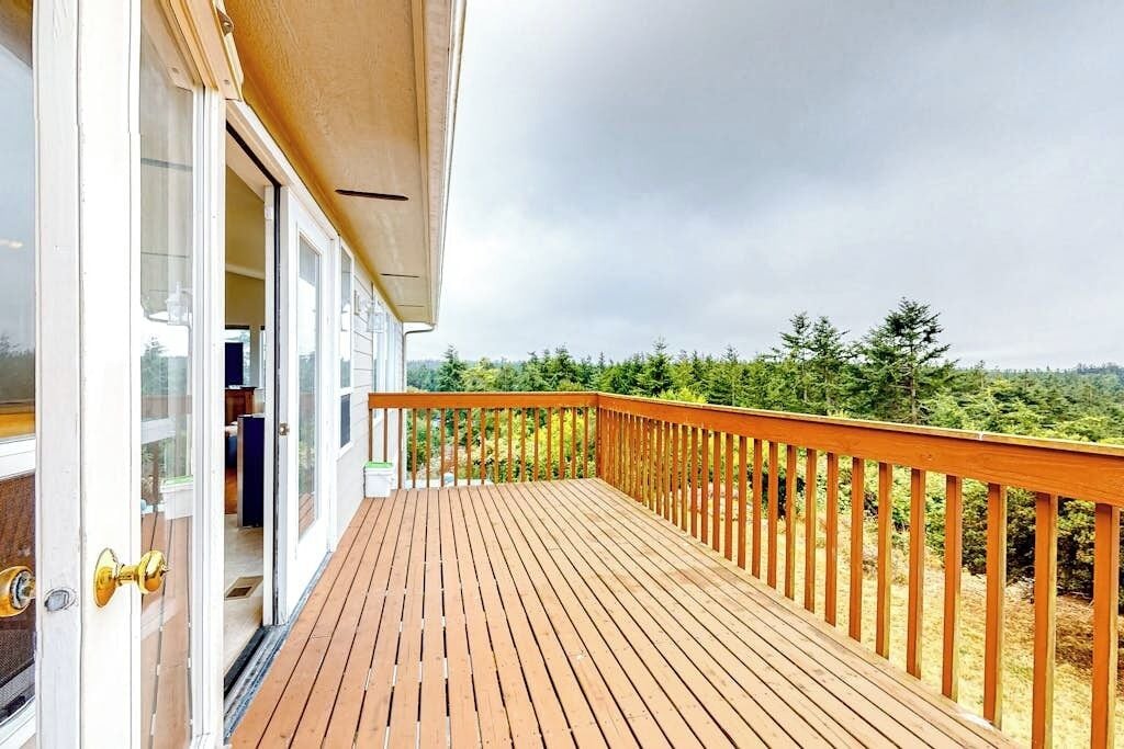 A wooden deck with a glass door leading to a room, surrounded by a forested landscape.