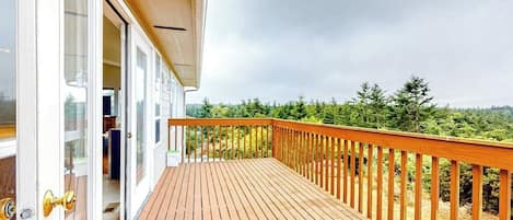 A wooden deck with a glass door leading to a room, surrounded by a forested landscape.