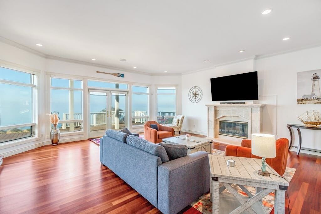 A spacious living room with a large sofa, a fireplace, and a television mounted on the wall.