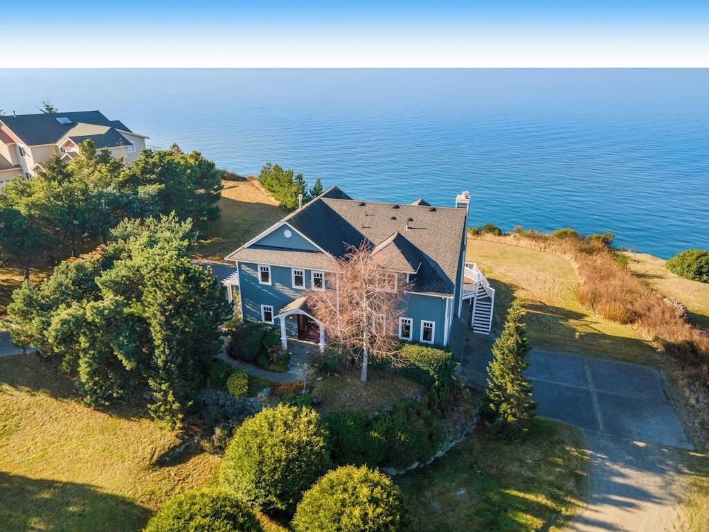 Une maison à deux étages avec une grande véranda à l’avant, entourée d’arbres et offrant une vue sur la mer.