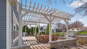 Un porche cubierto con una mesa, sillas, una jardinera de piedra y una estructura de pérgola.