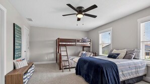 Un dormitorio con una cama litera, ventilador de techo, escalera, escritorio y ventana con persianas.