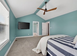 Ein Schlafzimmer mit einem Bett, einem Deckenventilator, einem an der Wand montierten Fernseher und einer Tür zu einem anderen Raum.