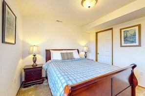A bedroom with a bed, two bedside tables with lamps, a door, and a framed picture on the wall.