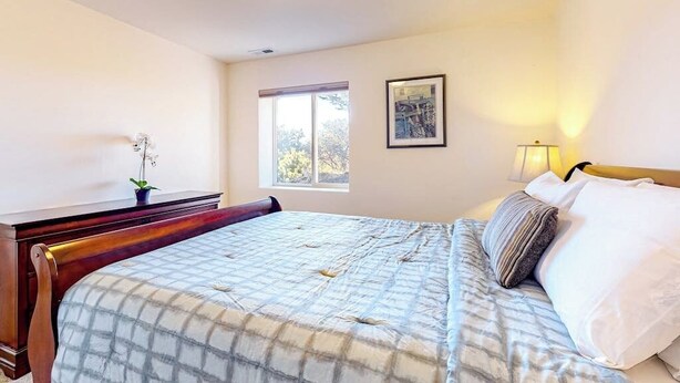 Un dormitorio con cama, mesita de noche, lámpara, ventana y un cuadro en la pared.