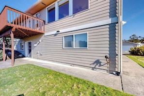 Une maison à deux étages avec une terrasse en bois, une porte d’entrée et une petite fenêtre.