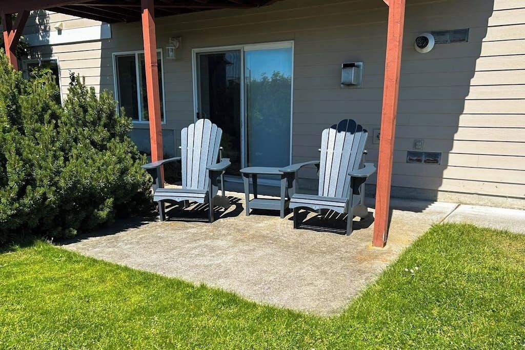 A covered patio with two Adirondack chairs and a small table, a sliding glass door, and a well-maintained lawn.