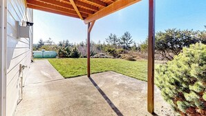 Un patio cubierto con piso de concreto, vigas de madera y vista a un césped verde y árboles.