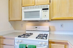 Une cuisine avec un four à micro-ondes blanc, une cuisinière et des armoires en bois.