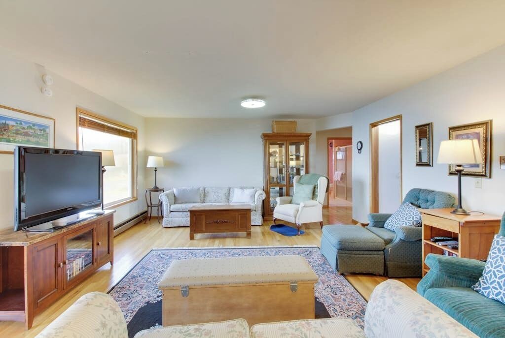 En rummelig stue med fjernsyn, sofa, lænestol og skammel.