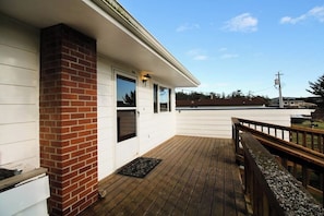A wooden deck with a brick chimney, white siding, and a metal railing.