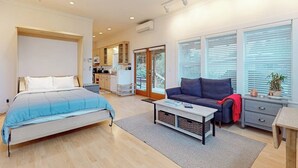 A modern bedroom with a bed, a sofa, a coffee table, and a view of a kitchen and balcony. - Restorative tiny home with amazing outdoor space, central location, and free Wifi (Langley)