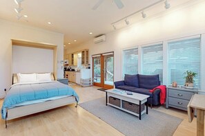Een moderne slaapkamer met een bed, een bank, een bijzettafeltje en uitzicht op een keuken en balkon.