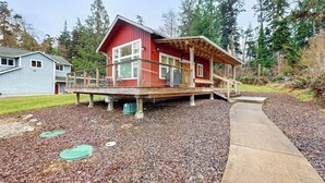 A red wooden house with a deck, a concrete pathway, and a surrounding wooded area. - Restorative tiny home with amazing outdoor space, central location, and free Wifi (Langley)