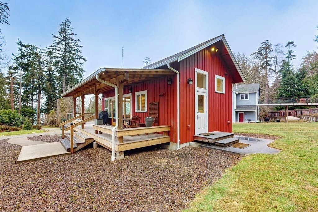 Een rode houten woning met een overdekte veranda, een voordeur en een kleine aanhangende garage.
