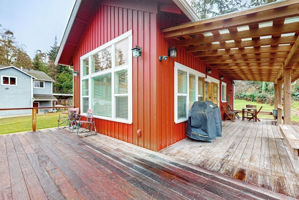 Een rood gebouw met een houten terras, tuinmeubels en een barbecue.