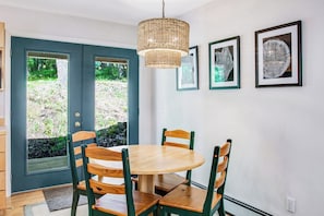 A dining area with a round table and four chairs, a hanging light fixture, and two framed artworks on the wall. - Dreamy Retreat in the Woods with Firepit, Fireplace, Free and Large Deck (Eastsound)