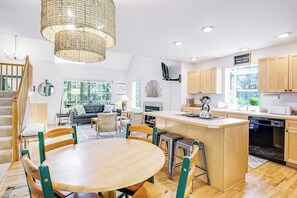 A modern kitchen with a central island, wooden cabinets, and a dining area with a round table and chairs. - Dreamy Retreat in the Woods with Firepit, Fireplace, Free and Large Deck (Eastsound)