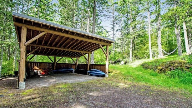 Un espace pique-nique abrité, accessible par un sentier de gravier, et entouré d’un paysage boisé.