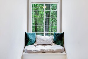 A window seat with a cushioned bench and two pillows, overlooking a forested area.