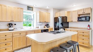 Une cuisine moderne avec des meubles en bois, un îlot central, des appareils électroménagers en acier inoxydable et une fenêtre qui laisse entrer la lumière naturelle.