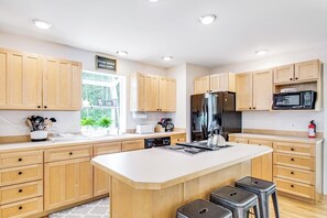 A modern kitchen with wooden cabinets, a central island, stainless steel appliances, and a window providing natural light. - Dreamy Retreat in the Woods with Firepit, Fireplace, Free and Large Deck (Eastsound)