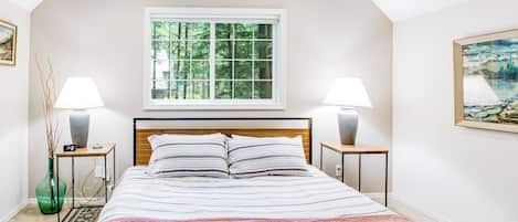 Ein Schlafzimmer mit einem Bett, zwei Nachttischen, einem Fenster und einem Bild an der Wand.
