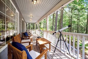 A covered porch with wooden furniture, a telescope, and a view of a forest.